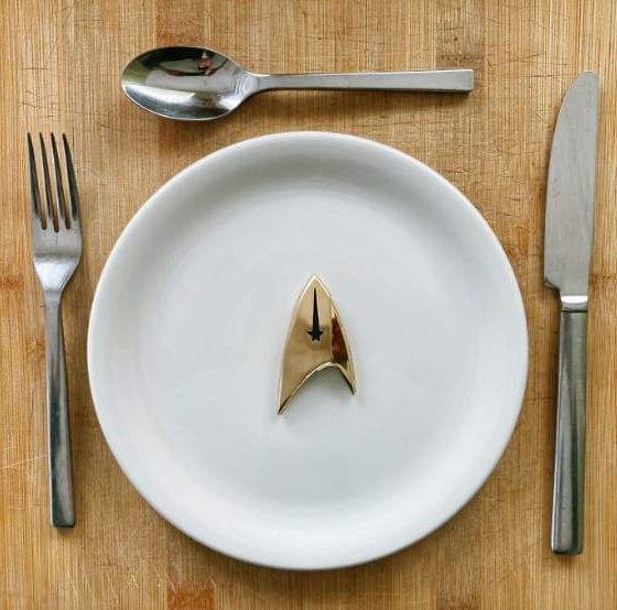 A gold Star Trek delta shield on a white plate with a knife, fork, spoon